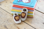 Inch Blue Leather Baby Shoes - Leo Cream stood upright against colourful books on wooden flooring