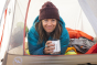 An adult lying down in a tent, holding their white Klean Kanteen Insulated 12oz Camping/Outdoor Mug