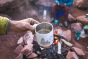 Close up of a hand holding the Klean Kanteen eco-friendly metal travel mug over a camp fire