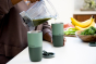 Close up of person pouring a green smoothie from a jug into a Klean Kanteen green stainless steel 16oz tumbler