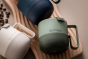 3 Klean Kanteen insulated steel mugs in the green, blue and beige colours on a brown wooden board