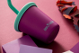 Close up of a Klean Kanteen kids stainless steel drinks cup in the grape colour on a pink background