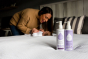 Close up of the Kokoso coconut oil lotion bottles on a white bed in front of a woman and a baby