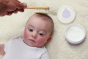 Close up of baby laying on a white fluffy background having its hair brushed with the Kokoso natural wooden hairbrush