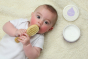 Close up of baby laying on a white fluffy blanket clutching the Kokoso natural wooden baby hairbrush
