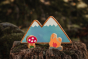 Close up of the Lanka Kade dan y ser campfire toy next to the Babipur moel mountains and toadstool on a wooden log