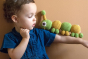 Boy stood in front of a beige wall with the Myum handmade crochet caterpillar toy balanced on his arm