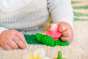 Close up of a baby's hand grasping the oli and carol natural rubber radish teething toy on a white carpet