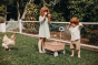 Girl and boy stood on some grass next to the Olli Ella light pink rattan wonder wagon toy 