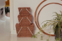 A stack of Olli Ella Piki Baskets, with the original on top, medium in the middle and large on the bottom. Stacked against a wall next to two bamboo hoops and a houseplant