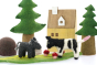 Close up of the Papoose felt cow and donkey toy figures on a Papoose play mat in front of some toy trees and wooden house