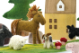 Close up of the Papoose felt toy horse, sheep and dog on a Papoose playmat in front of some toy trees and a yellow house