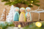 Peepul kids handmade wooden peg doll toys in the Holly, Mistletoe and Winter Berry designs on a wooden log in front of a Christmas tree