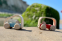 Plan Toys wooden vroom bus and vroom truck on some yellow sand in front of a green moss rock