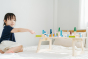 Young girl sat on a white bed pointing at the PlanToys eco-friendly wooden city blocks toy set