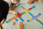 Close up of a family sat around the PlanToys rainbow wooden mood dominos game on a grey tablecloth
