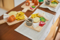 Close up of pieces from the PlanToys wooden charcuterie board toy set laid out on a white table cloth