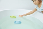Girl reaching out to touch a PlanToys natural rubber boat toy in a bath tub