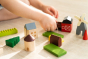 Close up of a childs hands moving pieces of the PlanToys solid wood country side blocks set on a wooden floor