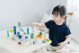 Young girl playing with the PlanToys plastic-free wooden city blocks on a white bed