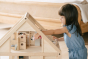 Close up of young girl leaning over to put a small doll toy inside the PlanToys handmade wooden dollhouse