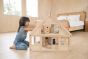 Young girl on her knees playing with the PlanToys eco-friendly dollhouse on a wooden bedroom floor