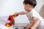Close up of young child making a stack with the PlanToys matching and nesting shapes on a grey bed