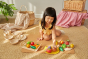Child on a mat playing with PlanToys fruit and vegetable tray and other play food sets. 