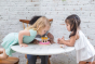 Three children at a table, blowing out the pretend candles of the PlanToys wooden birthday cake.