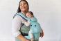 Woman stood with a baby inside a Tula explore baby carrier in the light blue robin colour