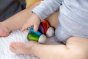 Plan Toys Rainbow Car Rattle Toy is a solid rubber wood sensory toy for babies painted in bright rainbow colours. Close up of baby playing.