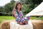 Girl sat on a bail of hay wearing the Frugi organic cotton flower power big snuggle suit