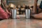 Close up of two people sat with Klean Kanteen plastic-free steel cups on a wooden table