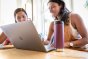 Close up of a 16oz Klean Kanteen reusable metal bottle in front of two girls using a laptop on a wooden table