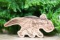 Reel wood wooden protoceratops dinosaur toy stood in front of a plant on a wooden floor