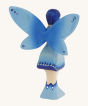 The back of the Bumbu Wooden Water Fairy Figure. The Water Fairy is coloured with hues of blue and silver on the wings, dress and boots, with inky blue hair, light blue eyes and pink lips. The Water Fairy is stood on a cream background