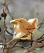 Lanka Kade brown wooden Wren toy figure, with a yellow beak and black feet, sitting on a dewy tree branch in the sun
