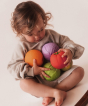 Toddler with an arm full of different fruit and vegetable Oli & Carol 100% Natural Rubber Baby Sensory Balls 