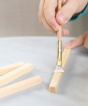 A close up of the gluing process. A child is painting glue onto the wooden sticks to build a WALACHIA wooden house