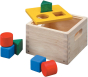 The Plan Toys Shape & Sort It Out is made with a natural wood finish with cut out handles at the sides, a yellow painted lid the square, circle, and triangle shape blocks in green, red and blue. White background. 