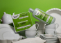 Box of Bio D eco friendly dishwasher tablets and bottle of Bio-D rinse aid on a green background balanced on white crockery