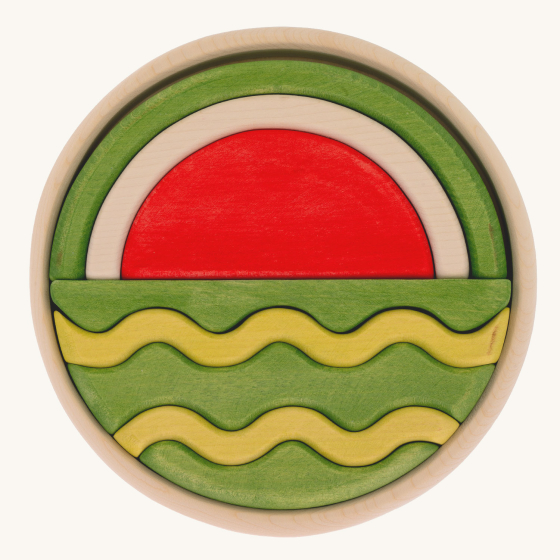 A round wooden puzzle depicting a watermelon in two halves. Different wooden shapes fit together to create the final puzzle. One half of the puzzle shows the inside of a watermelon whilst the other half shows the outside of a watermelon.