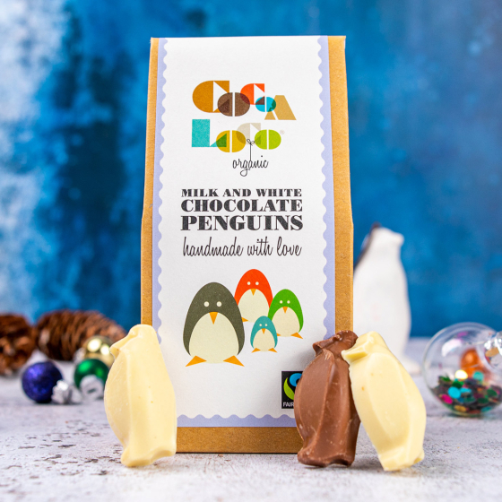3 Cocoa Loco organic white and milk chocolate penguins leaning against their box on a blue and white Christmas background
