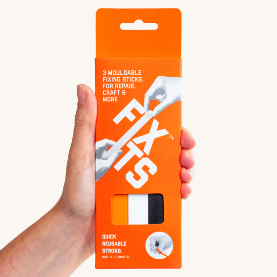 Close up of hand holding a 3 pack of FixIts plastic fixing strips on a beige background
