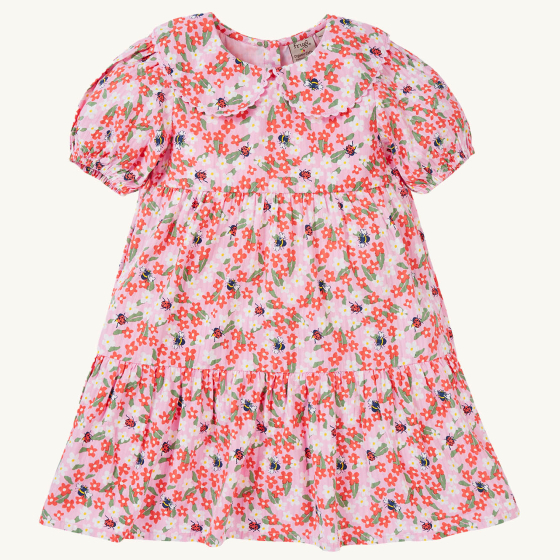 The front of the Frugi GOTS organic cotton Matilda Collared Dress - Pink Floral Fun. A playful spring-time print of white and red flowers, bees and ladybirds on a light pink fabric. The dress is a Tiered Dress with oversized peter pan collar and puff slee