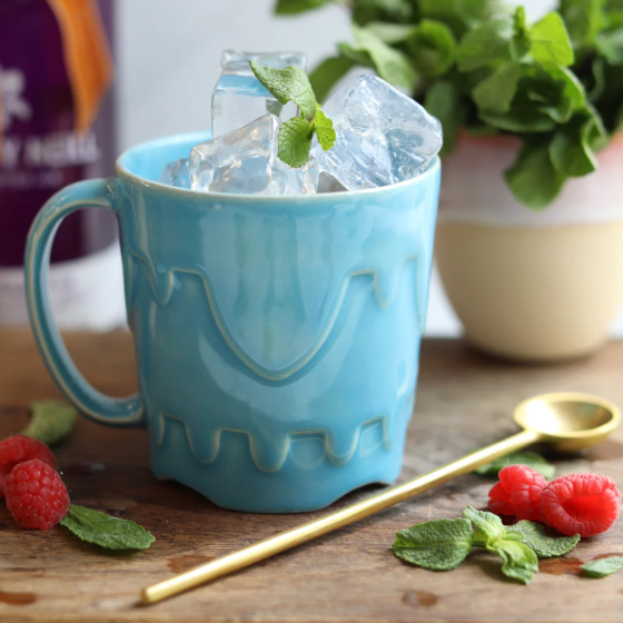 Glosters handmade Sandcastle Mug - Coast-Blue. The mug sits on a wooden table, it is full of ice and has fruit and mint in front of it.