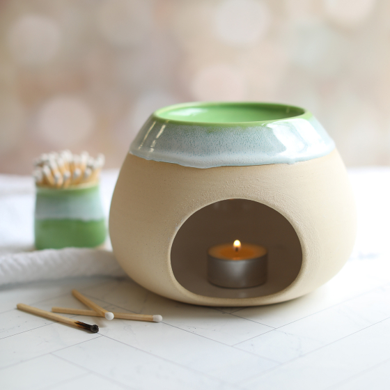 Glosters Ceramic Wax Melt Burner is beautifully showcased in a home setting, on a white herringbone patterned table. With a Pea Green coloured indent glaze surrounded by a foamy white glaze mimicking sea waves crashing against the shore.
