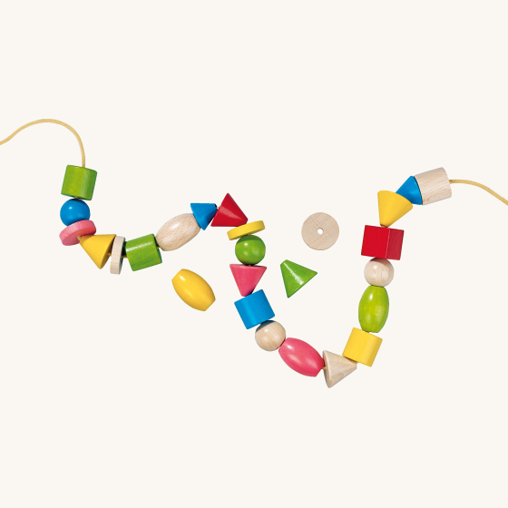 HABA Wooden Assorted Threading Bambini Beads. A colourful selection of different shaped wooden beads in natural wood and glossy textures which have been threaded on a yellow cord, on a cream background