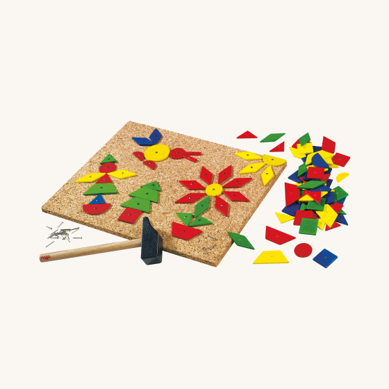HABA Large Geo Shape Tack Zap Game. A fun construction game with various shames in red, blue, green and yellow which comes with a cork tacking board, a wooden hammer and tacking nails, on a cream background