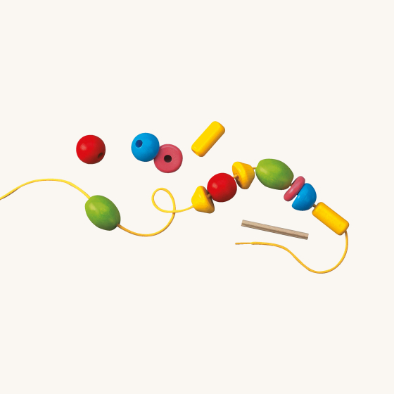 HABA Bambini Beads. A colourful assortment of beads in different shapes and sizes, with a yellow cord, on a cream background